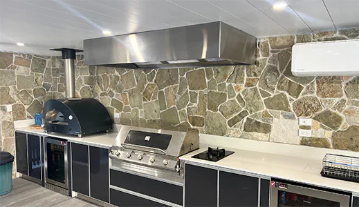 A beautiful stainless alfresco rangehood against a stone wall, adding a touch of elegance to the outdoor cooking area
